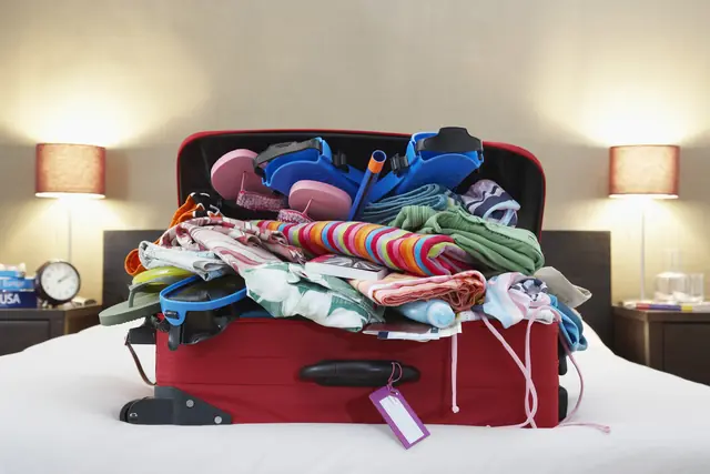 Valise ouverte remplie de vêtements posée sur un lit d’hôtel